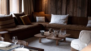Een gezellige woonkamer met een bruine bank, een houten salontafel en een eethoek met een tafel gedekt voor twee personen.