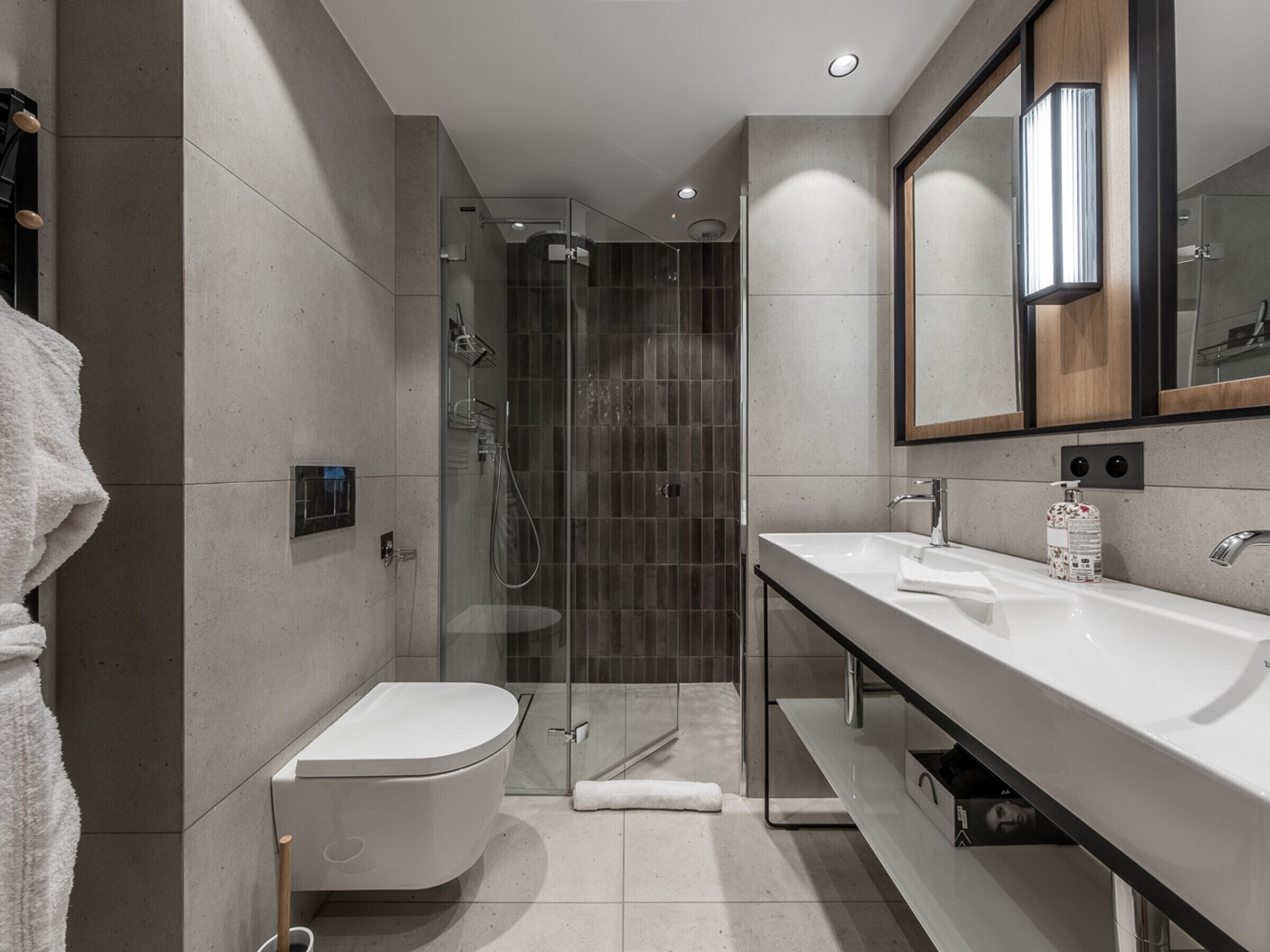 A modern bathroom with a glass-enclosed shower, a white toilet, and a large mirror above the sink.
