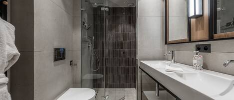 A modern bathroom with a glass-enclosed shower, a white toilet, and a large mirror above the sink.