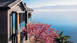 A traditional building with a modern glass extension overlooking a calm lake and mountains. - Yakamoz Erhai Hotel (Dali)