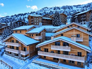 Un ensemble de chalets en bois dotés de balcons, entourés d’arbres couverts de neige et avec une chaîne de montagnes en toile de fond.