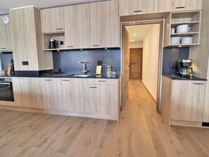 Une cuisine moderne avec des meubles de rangement en bois, un four encastré et une machine à café.