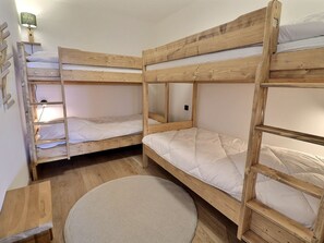 A bunk bed room with a wooden floor, a round rug, and a wall-mounted lamp. - Beautiful 4-room cabin, 8 people, sauna, parking, Méribel (Méribel)