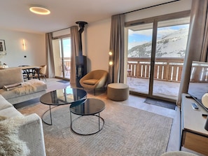 Una sala de estar moderna con chimenea, un sofá, una mesa de centro redonda y un balcón con vista a una montaña nevada.