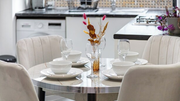 A dining table set with white plates, bowls, and wine glasses, centered with a decorative vase. - |Modern Two Bed Apt with free Gated Parking Space| (London)