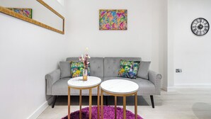A modern living room with a grey sofa, two round tables, colorful artwork, and a wall clock. - |Modern Two Bed Apt with free Gated Parking Space| (London)