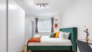 A modern bedroom with a green bed, white bedding, and a small desk with a chair. - |Modern Two Bed Apt with free Gated Parking Space| (London)