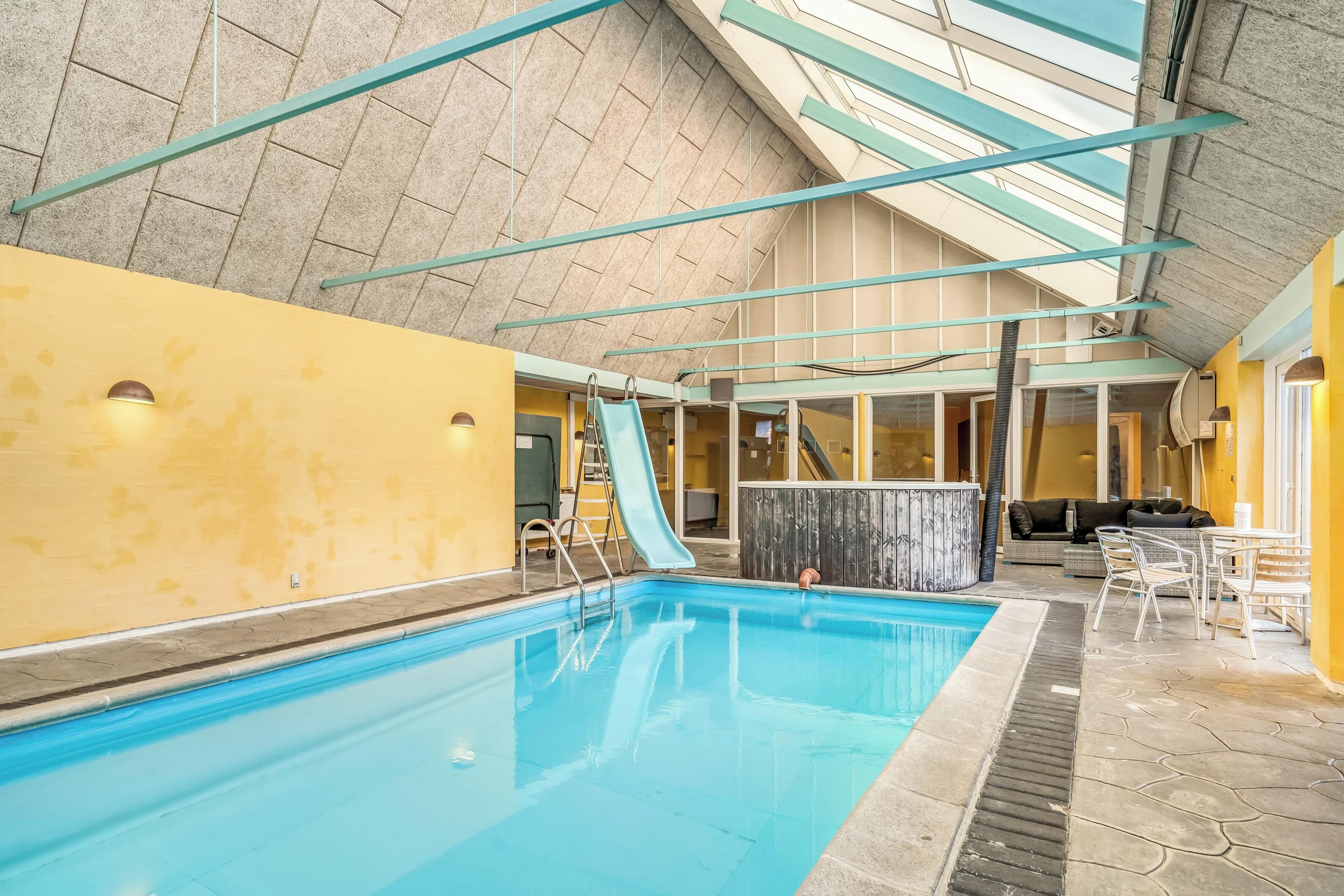 Une piscine intérieure avec un toboggan, un jacuzzi et un espace détente avec des chaises et une table.