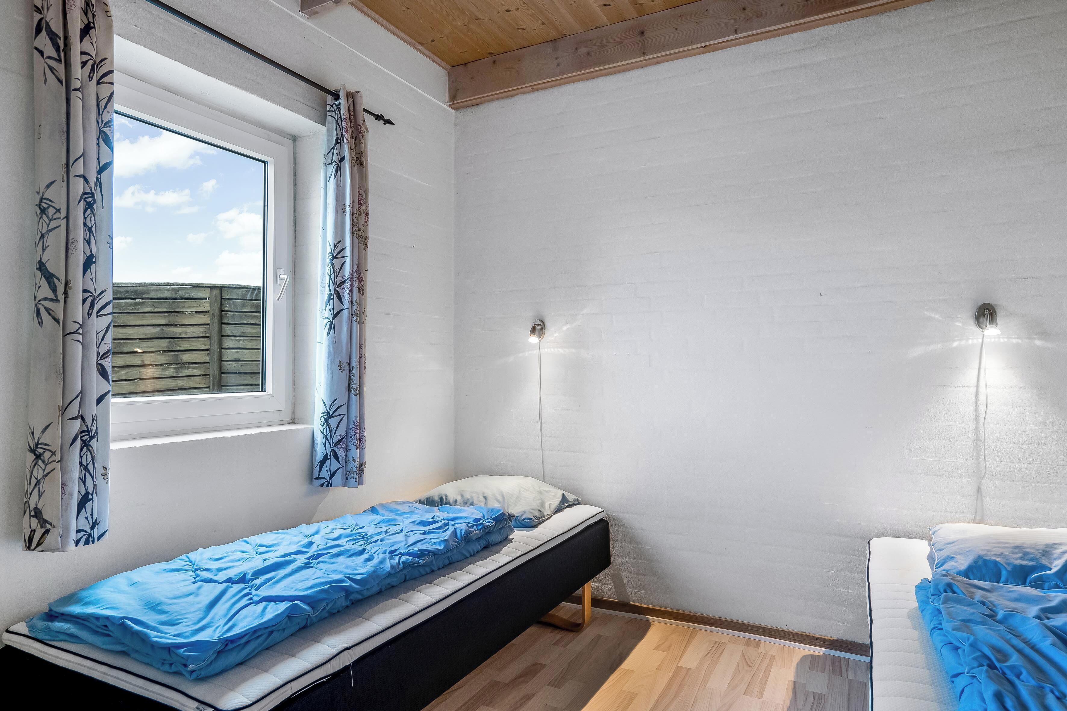 A room with two single beds, a window with curtains, and a white brick wall.