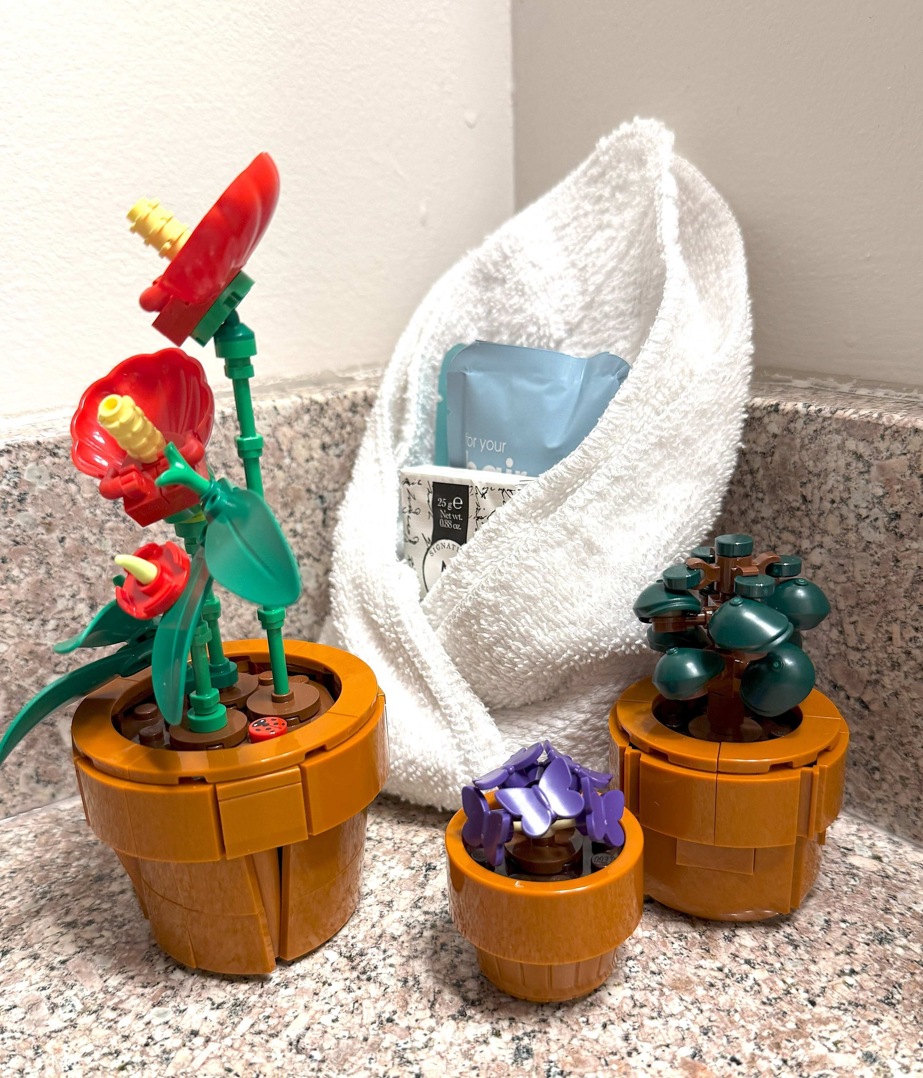 A kitchen counter with three potted plants, a white towel, and a blue bag.