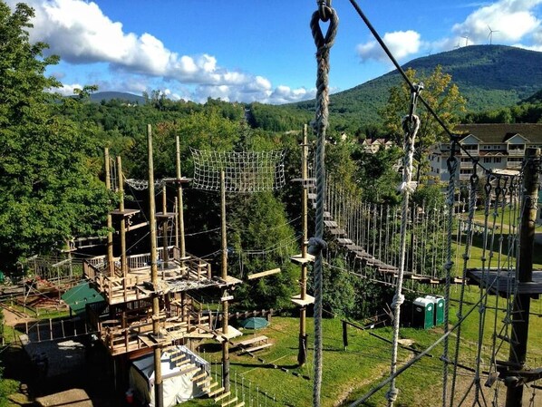 Parque de aventuras al aire libre con puentes de cuerda, estructuras de madera y montañas al fondo.