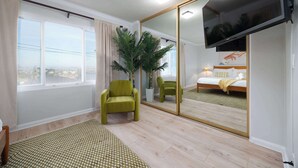 Habitación de hotel con cama, un sillón verde, un espejo grande y vistas a la ciudad desde la ventana.