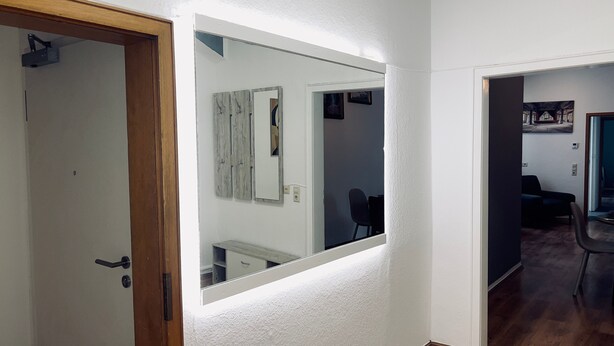 A hallway with a large mirror reflecting a room with a chair and a painting on the wall. - Cozy Koblenz Apartment With City Views (Koblenz)
