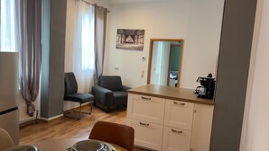 A small, modern room with a dining area, a sofa, a coffee machine, and a painting on the wall. - Cozy Koblenz Apartment With City Views (Koblenz)