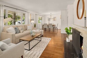 Een moderne woonkamer met een bank, salontafel en open haard. Er is een eethoek met een tafel en stoelen.