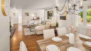 Una sala de estar moderna con comedor, que presenta una mesa de madera dispuesta para cuatro personas, un sofá y una araña.