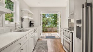 Una cocina moderna con muebles blancos, electrodomésticos de acero inoxidable y vistas a un patio trasero a través de una puerta abierta.