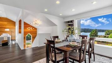 A modern dining area with a wooden table and chairs, a vase with flowers, and a view of a lake through large windows.