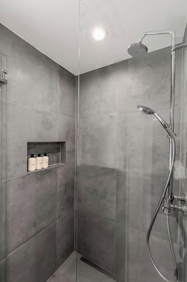 Una ducha moderna con puerta de cristal, repisa empotrada con artículos de aseo y cabezal de ducha manual.