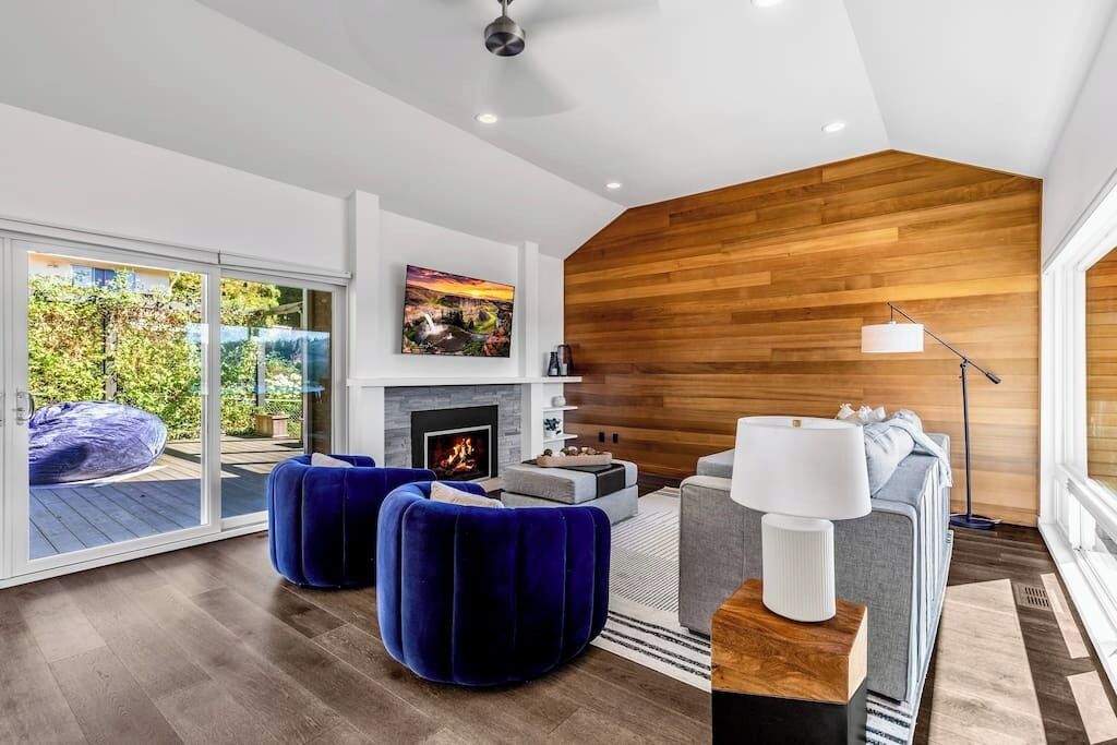 A modern living room with a fireplace, a sofa, and a blue ottoman.