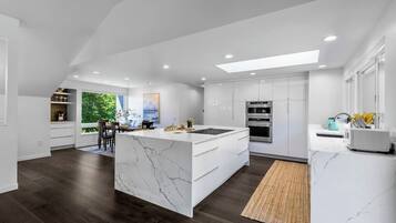 A modern kitchen with white cabinetry, a marble island, and a large window overlooking greenery.
