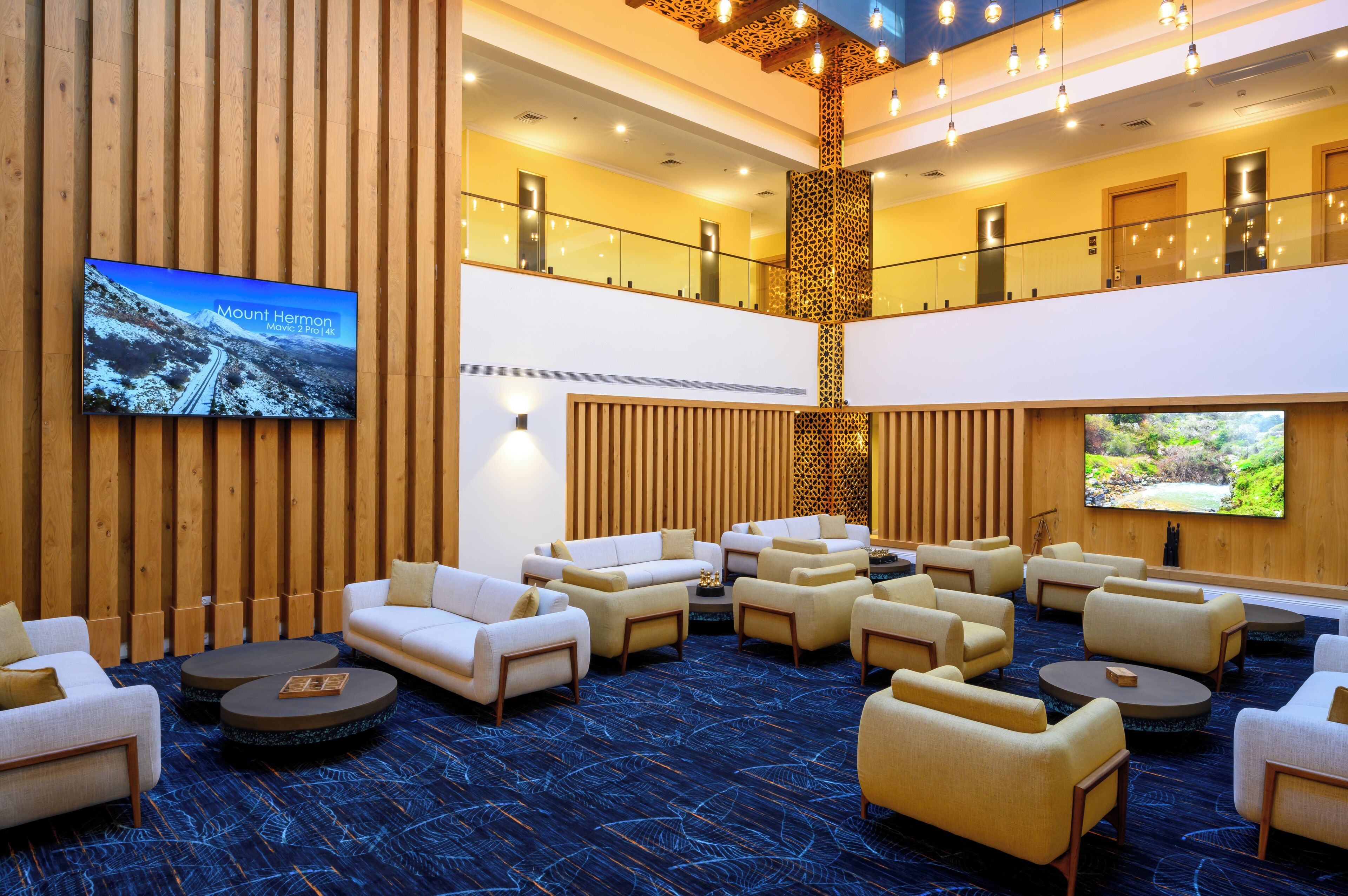 A spacious lobby with multiple seating areas, a large screen displaying a movie, and a high ceiling with decorative lighting.