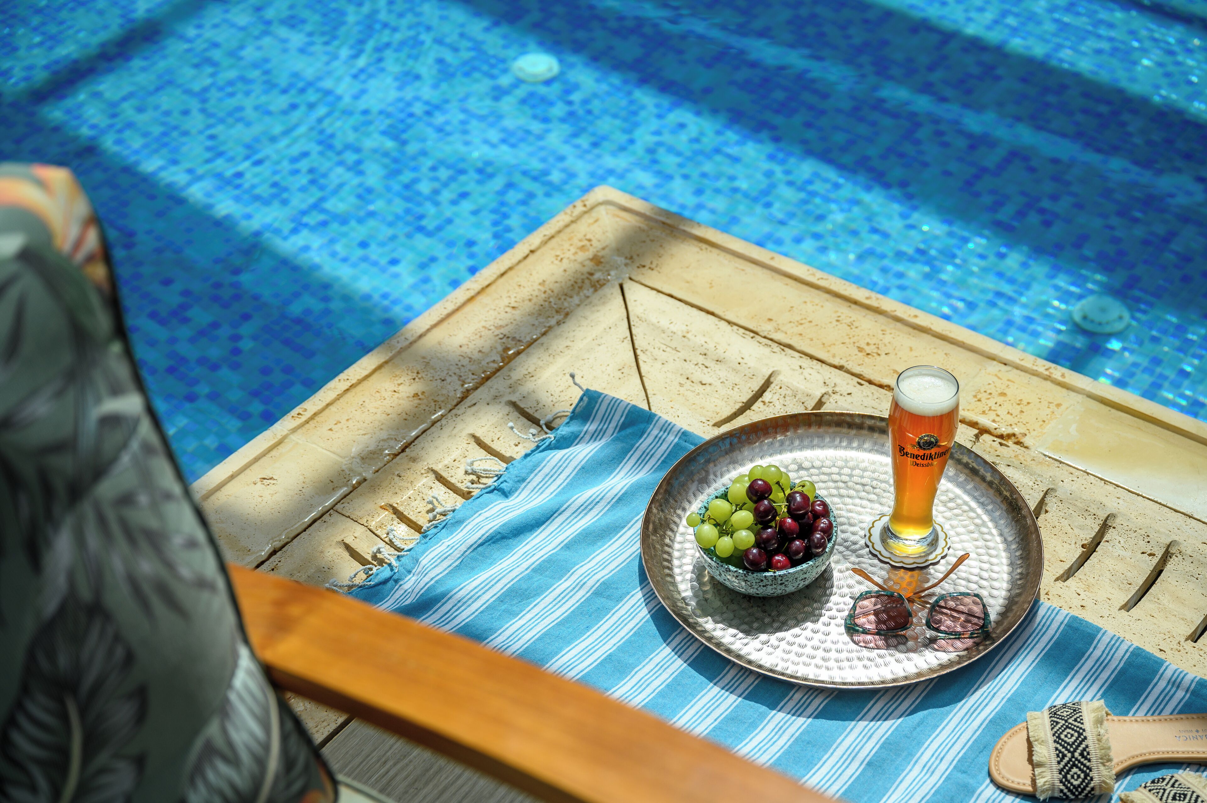 Una mesa con una bandeja que contiene una cerveza en un vaso, un cuenco de uvas y un par de gafas de sol.