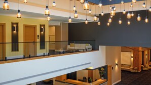 Un hall de hotel con mostrador de recepción, una zona de estar con sofás y una escalera que conecta los pisos.
