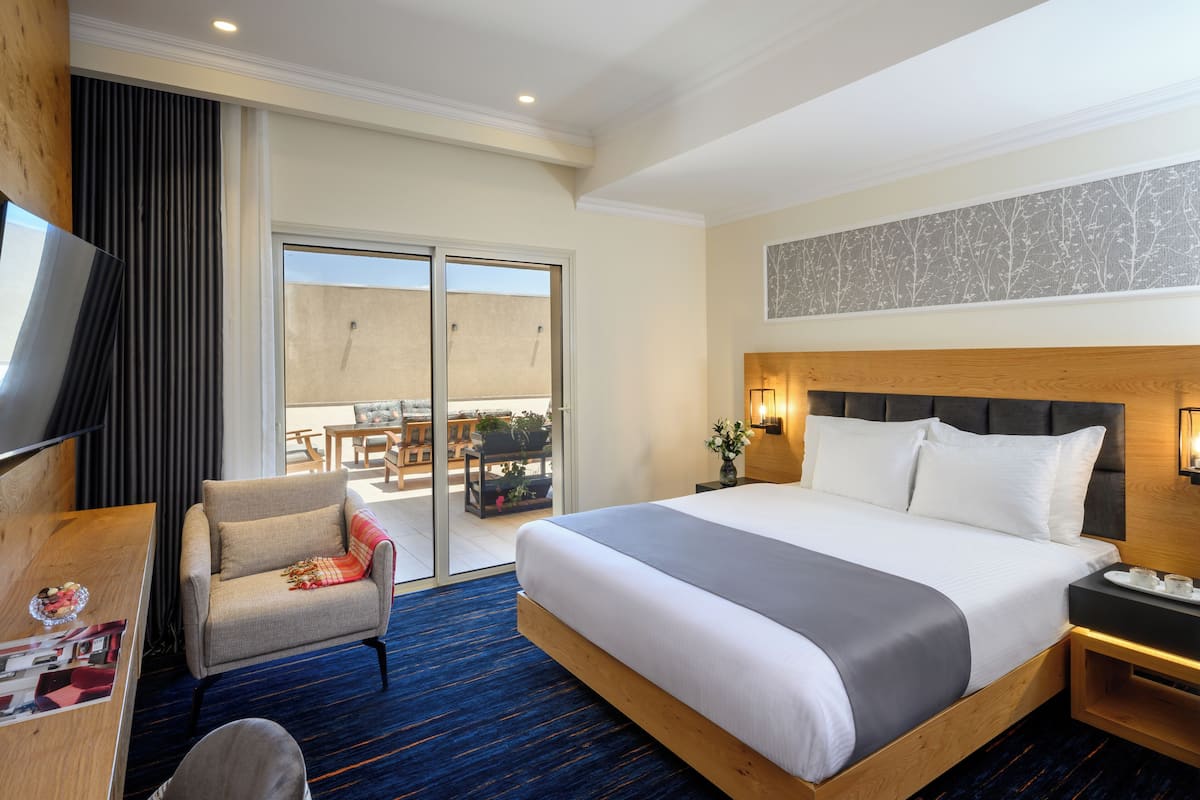 Ein Hotelzimmer mit einem großen Bett, einem Schreibtisch, einem Sessel, einem Fernseher und einem Balkon mit Sitzgelegenheit.