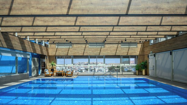 Una piscina interior con baldosas azules cristalinas, sillas de descanso y vistas a la ciudad.