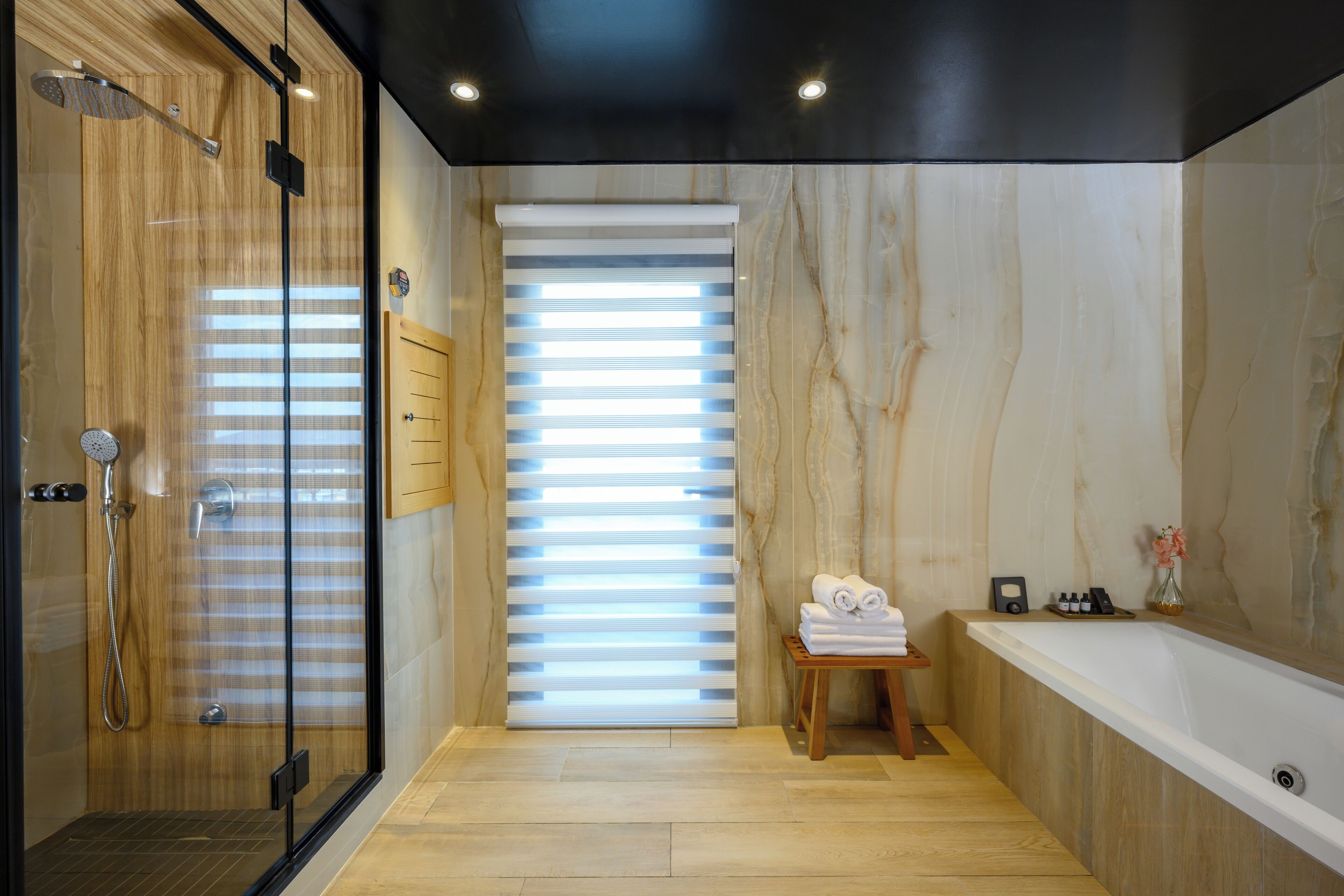 Un baño moderno con cabina de ducha de vidrio, tocador de madera, una bañera grande y una ventana con persianas.