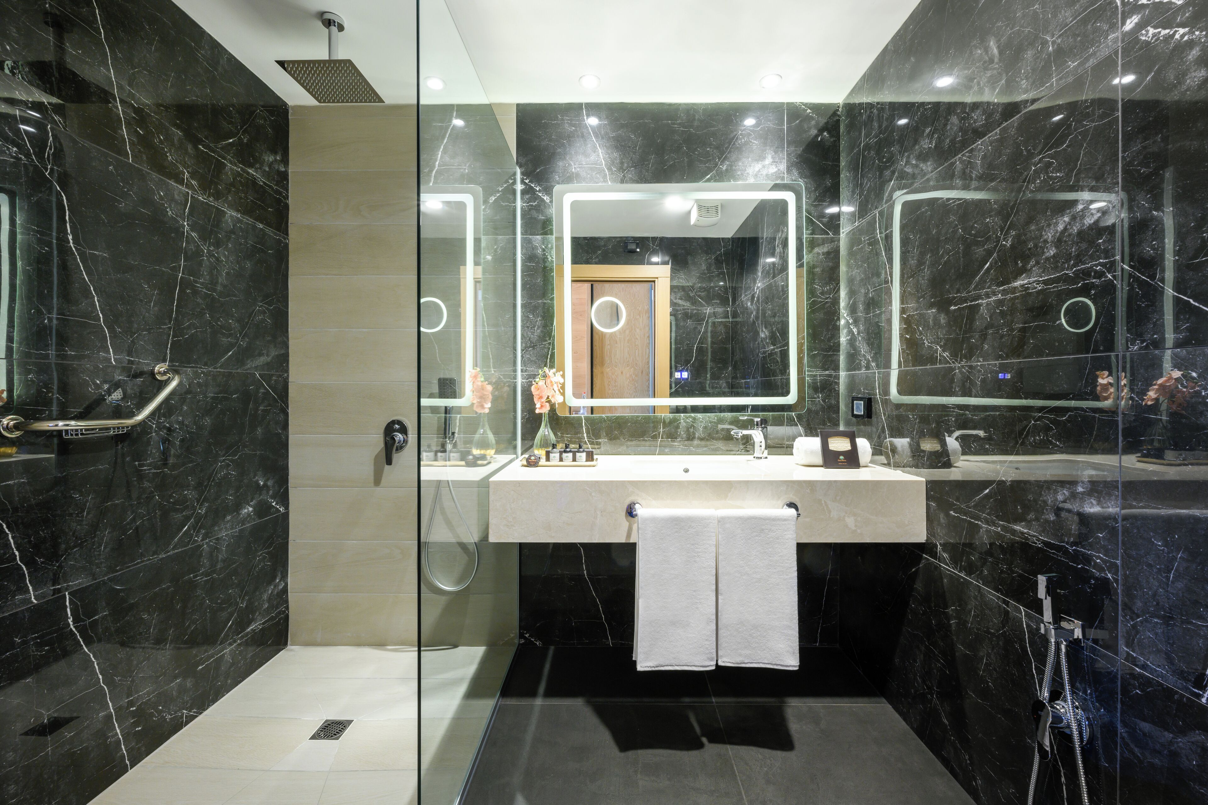 Een moderne badkamer met een douchecabine van glas, een marmeren wastafelmeubel en een grote spiegel met ingebouwde verlichting.