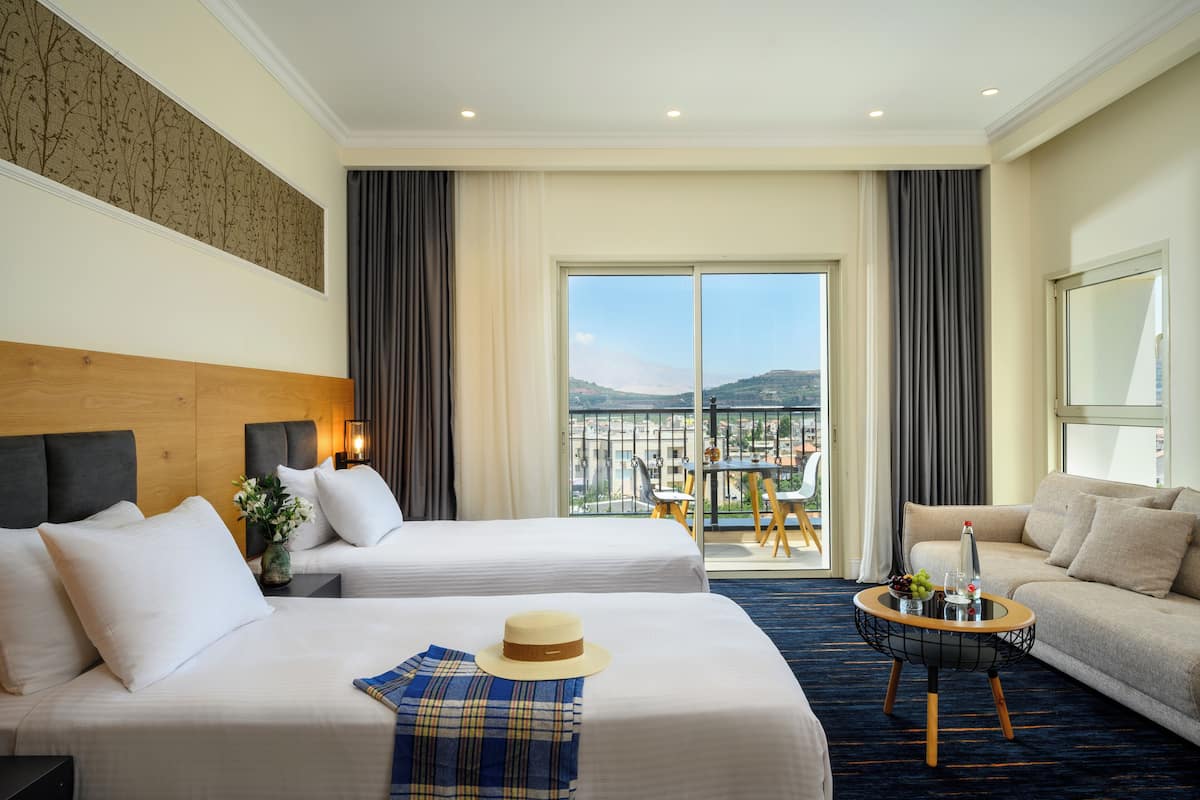 Ein Hotelzimmer mit zwei Betten, einem Schlafsofa, einem Balkon mit Aussicht und einem Essbereich.