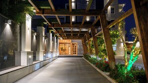 Un paseo techado con estructura de madera, paneles de vidrio y una puerta que da a un edificio.