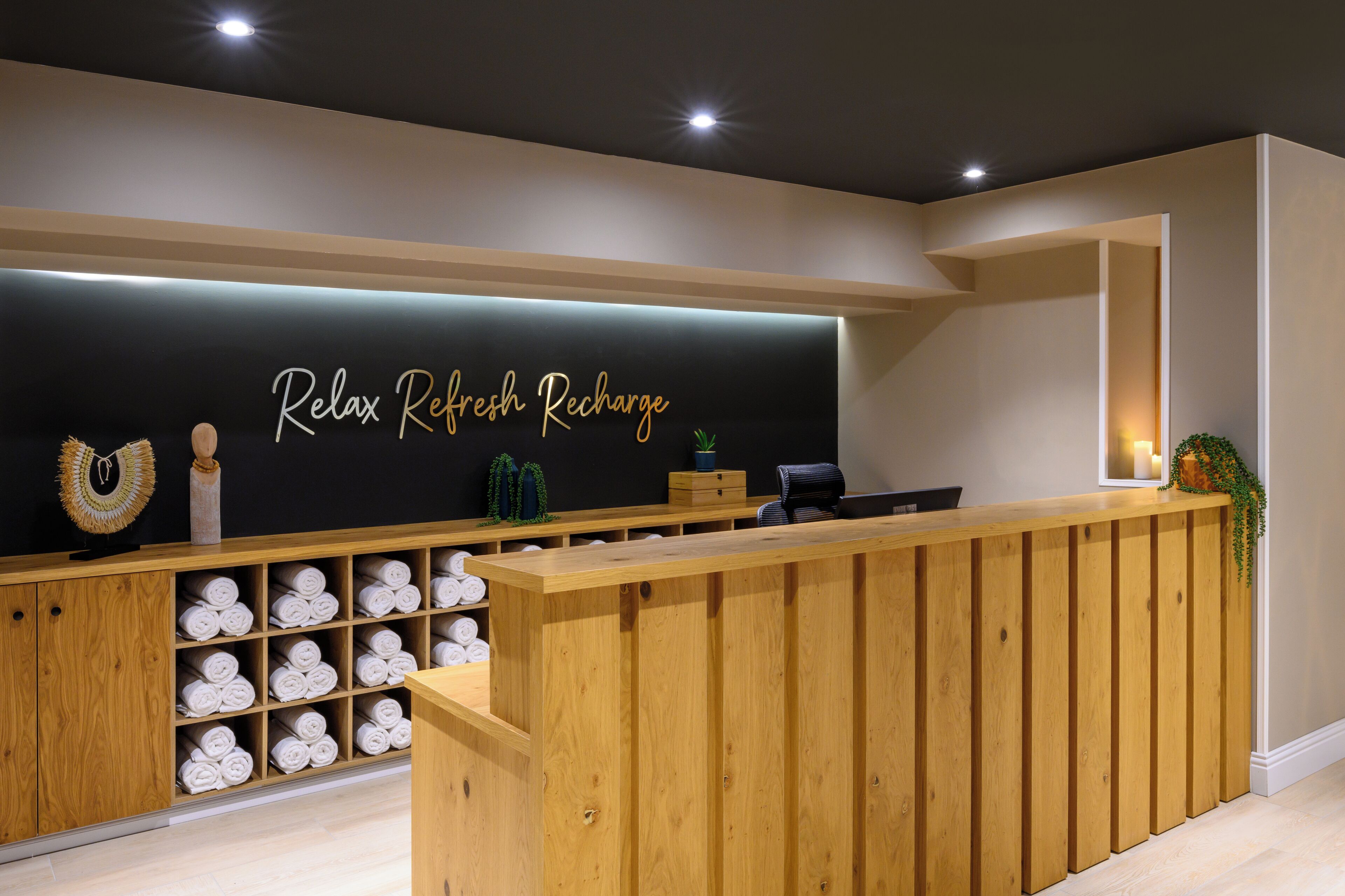 A reception desk with a sign reading "Relax Refresh Recharge" and a wooden counter with towels.