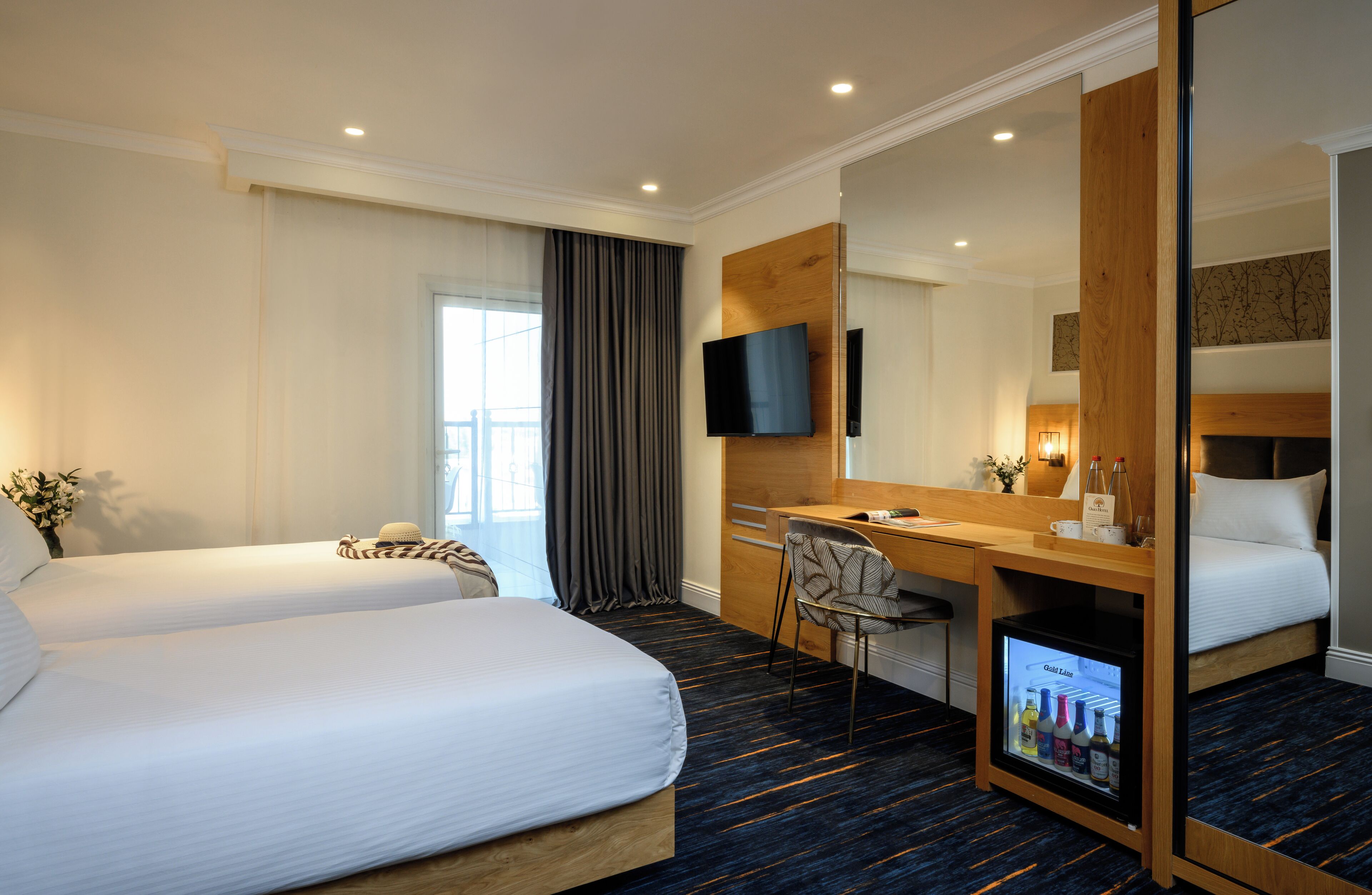 A hotel room with two beds, a desk, a chair, a TV, and a minibar.