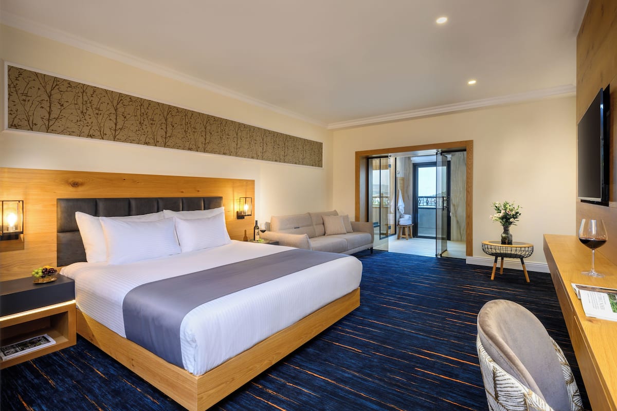 Ein Hotelzimmer mit einem großen Bett, einem Sofa, einem Schreibtisch mit einem Weinglas und einem Fernseher.