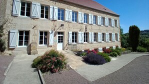 Ein zweistöckiges Steinhaus mit weißen Fensterläden, einem roten Dach und einer gepflasterten Auffahrt mit Blumenbeeten.