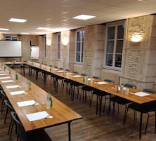 Un salón de conferencias con largas mesas, sillas, una pantalla de proyector y una pizarra.