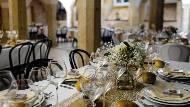 Ein Restaurant mit gedeckten Tischen, weißen Tischdecken, Weingläsern und einer Blumenarrangements als Dekoration.