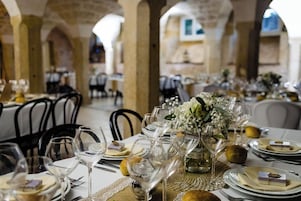 Un restaurante con mesas dispuestas para comer, con manteles blancos, copas de vino y un centro de mesa con flores.