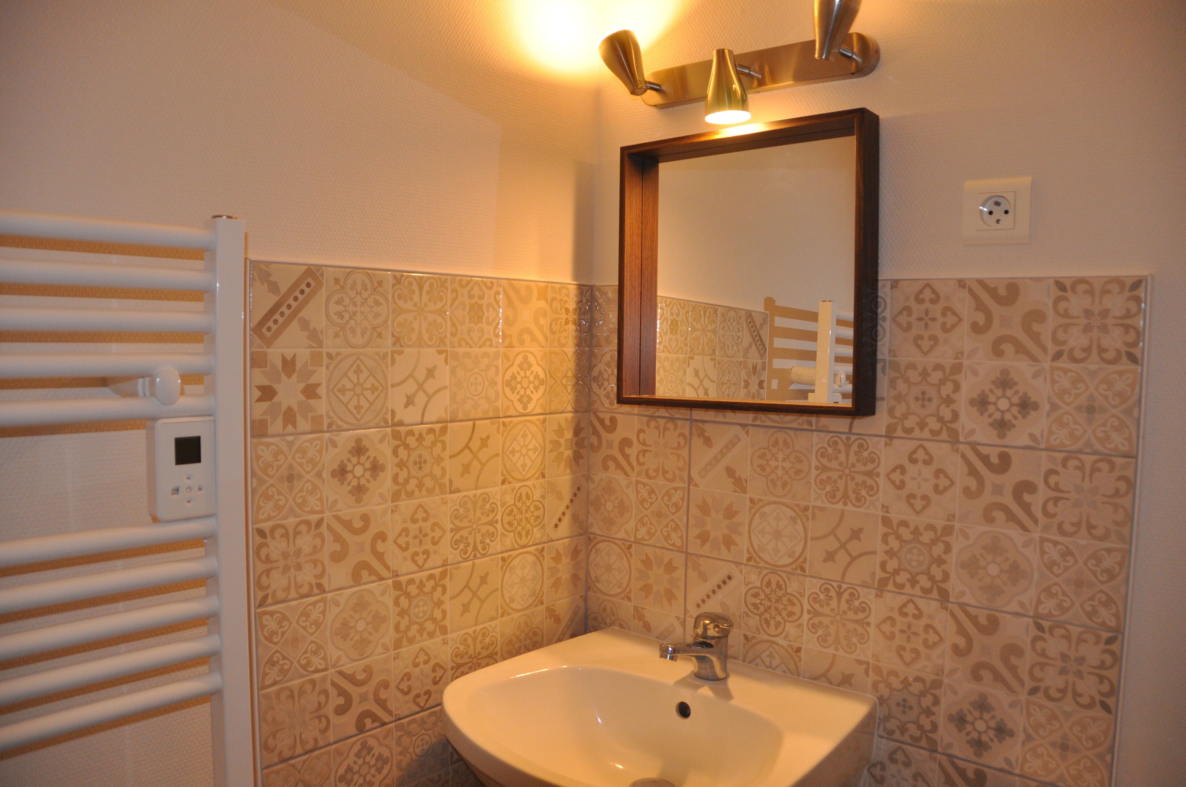 A bathroom with a white sink, a mirror, and patterned tiles.