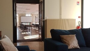Ein modernes Wohnzimmer mit einem dunkelblauen Sofa und einem beigen Kissen, einem Holzboden und Blick auf einen Konferenzraum mit einer Whiteboard und Stühlen.