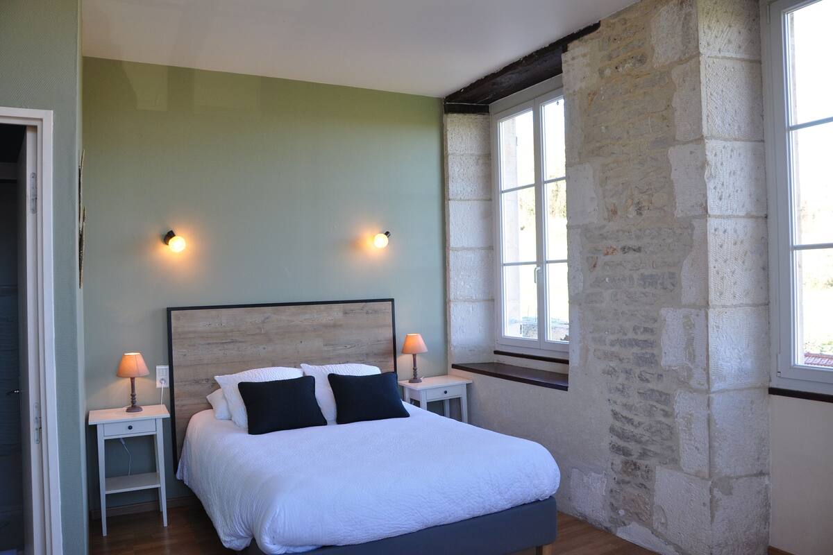 A bedroom with a bed, two bedside tables, two lamps, and a stone wall.