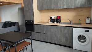 Une cuisine compacte équipée d’un four encastré, d’une machine à café, d’une bouilloire et d’un lave-linge.