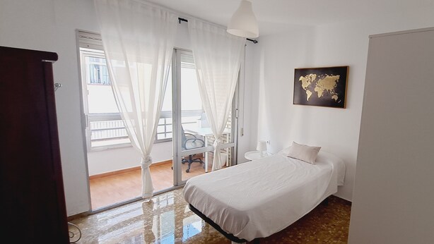 Een hotelkamer met een bed, een bureau, een stoel, een wereldkaart aan de muur en een balkon met uitzicht.