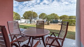 Eine überdachte Terrasse mit einem runden Tisch und vier Holzstühlen, mit Blick auf eine grüne Fläche mit Bäumen und eine entfernte Ansicht von Gebäuden.