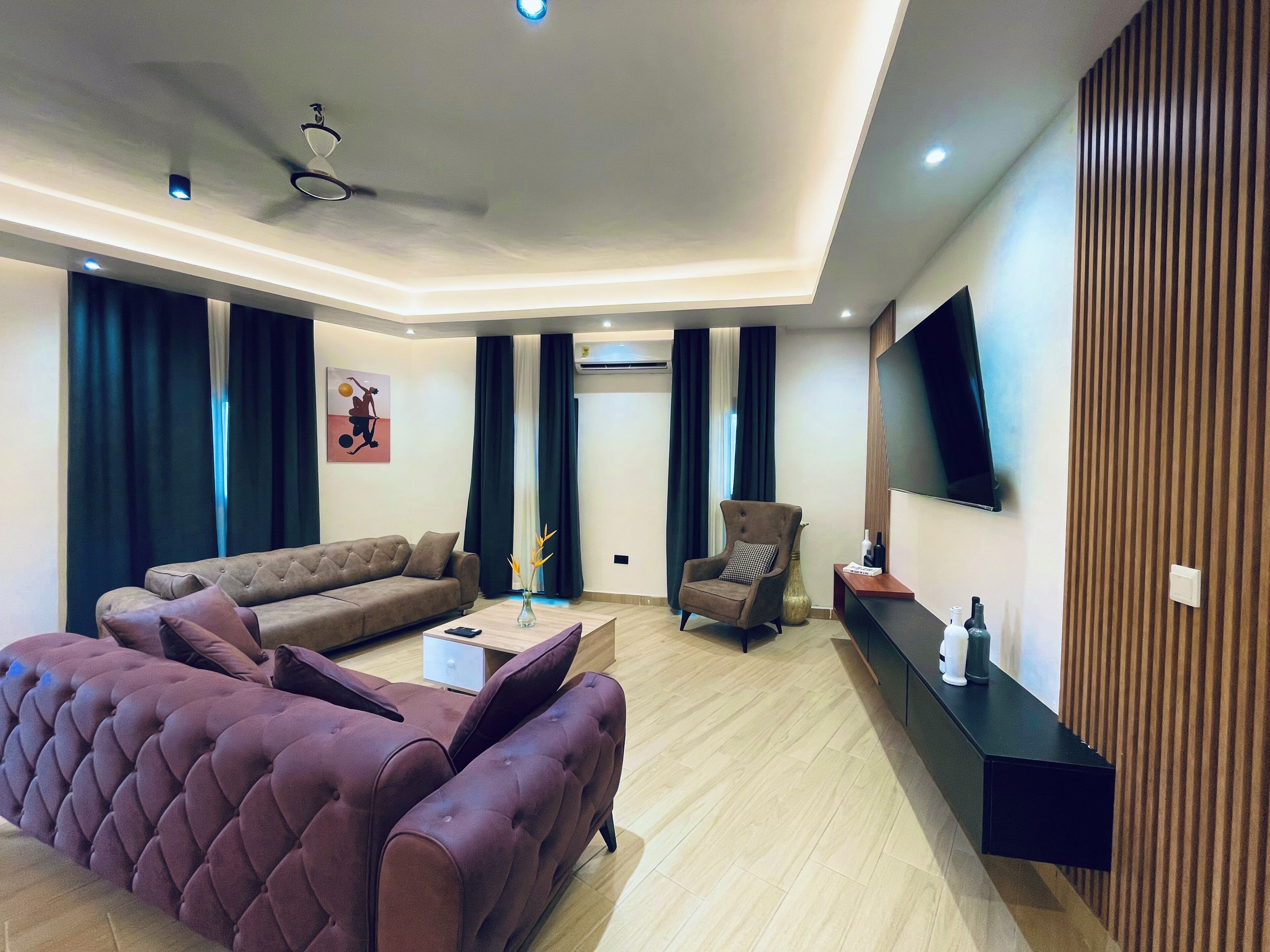 A modern living room with a sofa, armchair, and a flat-screen TV mounted on the wall.