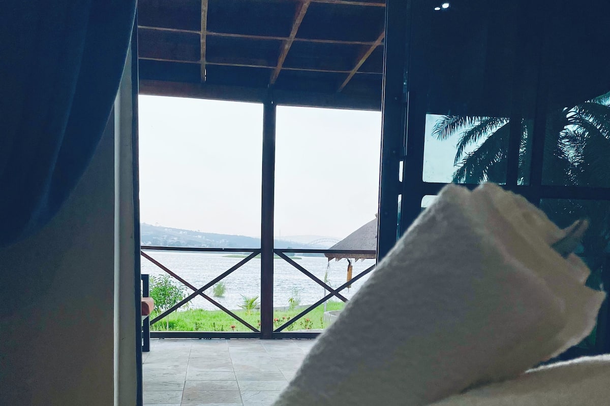 A bed with white linens and a view of a balcony with a railing and greenery.
