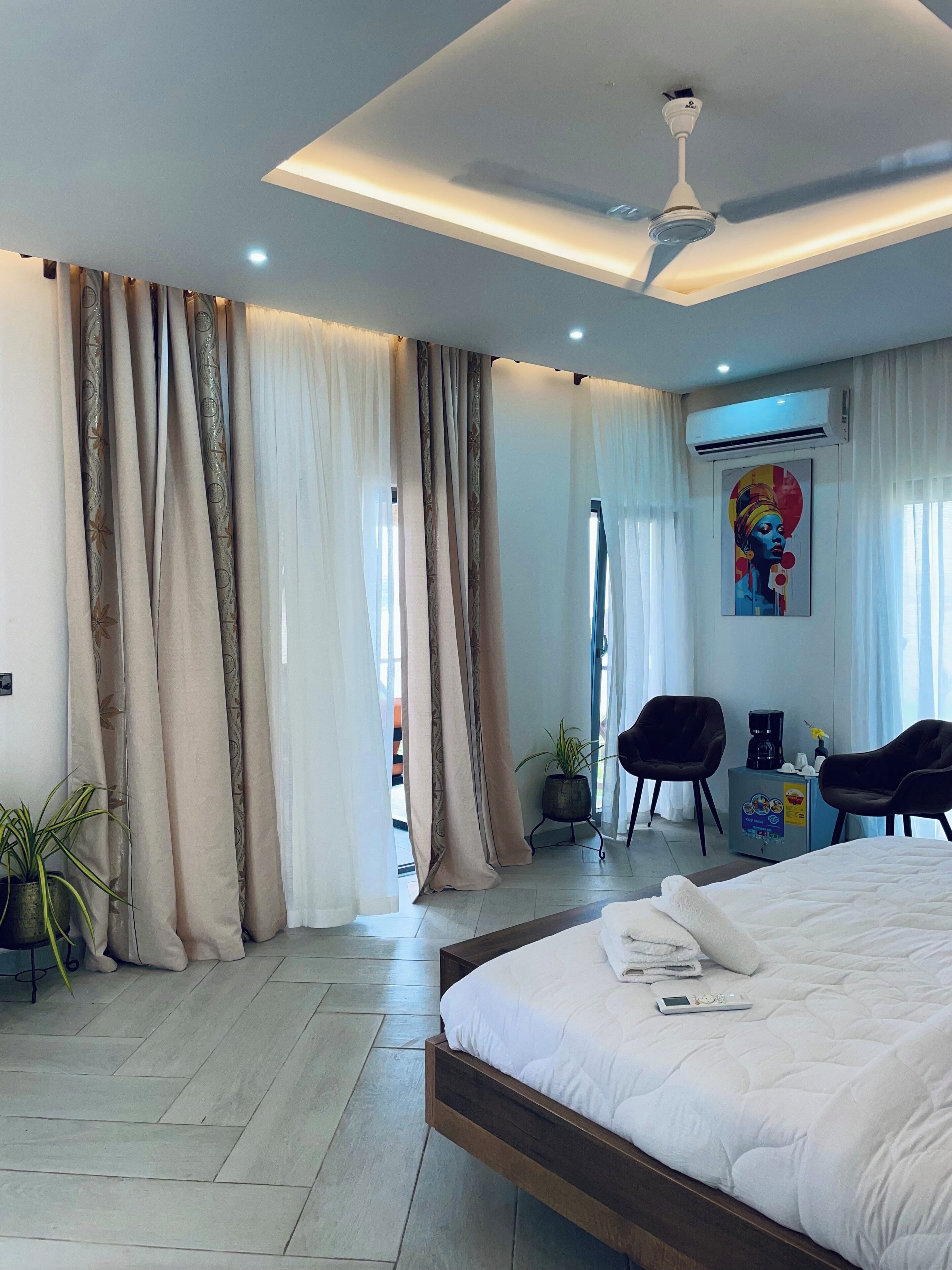 A modern hotel room with a large bed, a ceiling fan, and a view of the outdoors.